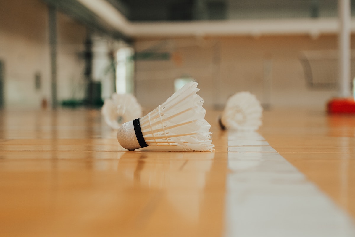 Ground level of similar plastic shuttlecocks reflecting on bright shiny floor with marking line